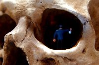 A small figure of a person walks into the eye socket of a skull, holding a lantern.