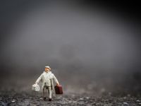 Photograph of a miniature person walking while carrying bags.